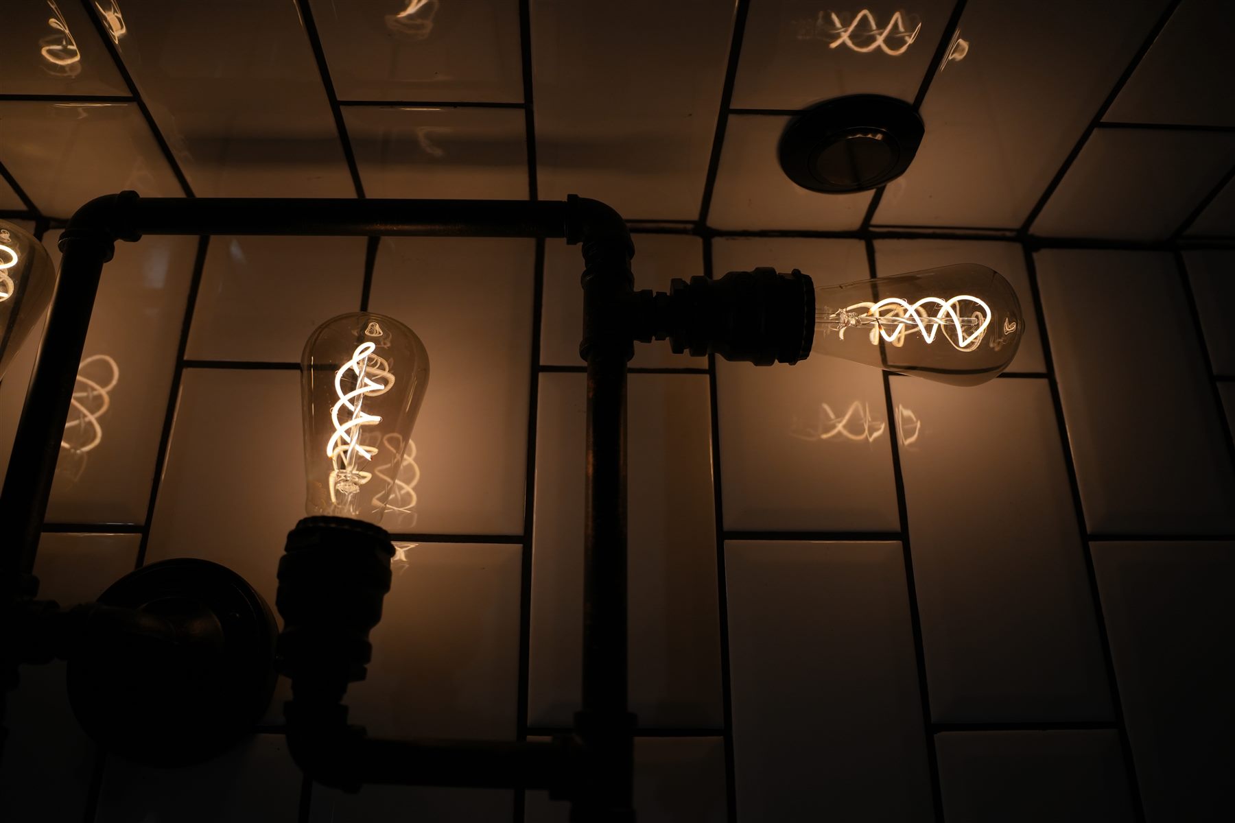 Subway-tiled ceiling with exposed pipes and vintage bulbs